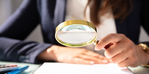 Close-up Of A Businesswoman's Hand Looking At Contract Form Through Magnifying Glass