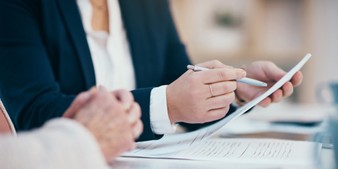 Hands working, reading and writing on business meeting notes in an office boardroom. Closeup view of corporate executive team doing work. Management group looking through finance data together