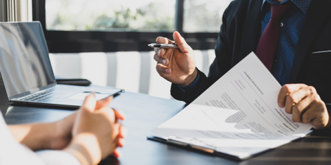 Businessman in suit in his office showing an insurance policy and pointing with a pen where the policyholder must to sign. Insurance agent presentation and consulting insurance detail to customer.