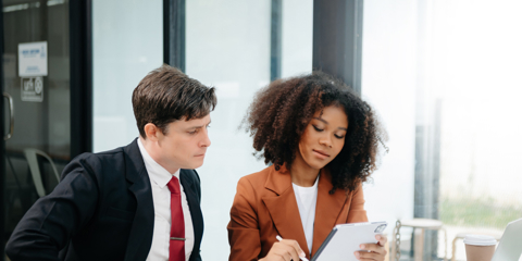 Businesswomen work and discuss their business plans. A Human employee explains and shows her colleague the results paper in office.