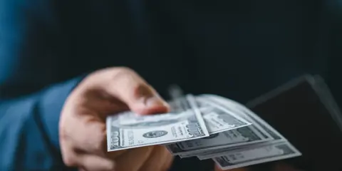Close-up of a person handing over US dollar bills. Concept of payment, transaction, finance, banking, and cash handling.
