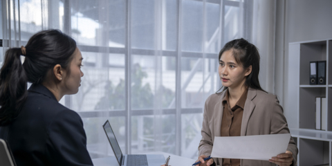 Two asian businesswomen discussing business strategy and financial charts in an office meeting