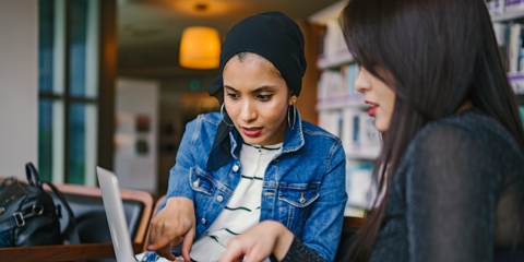 two women discussing business while pointing at laptop