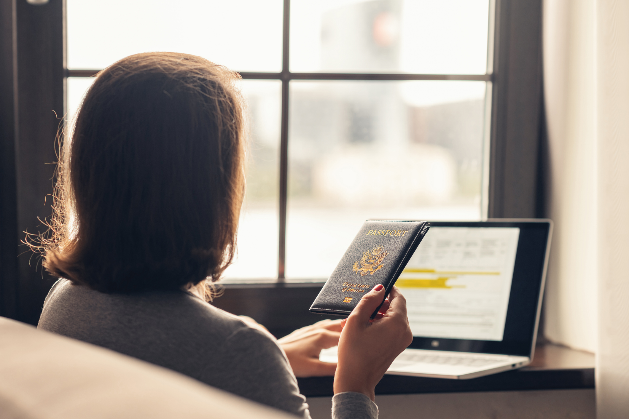 Woman holding passport filling visa application form on the laptop. Online and home work concept.