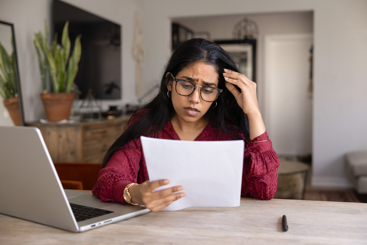 Frustrated concerned young Indian woman in glasses reading bad news in legal document, getting financial problems, rejection from university, notice from bank, touching head