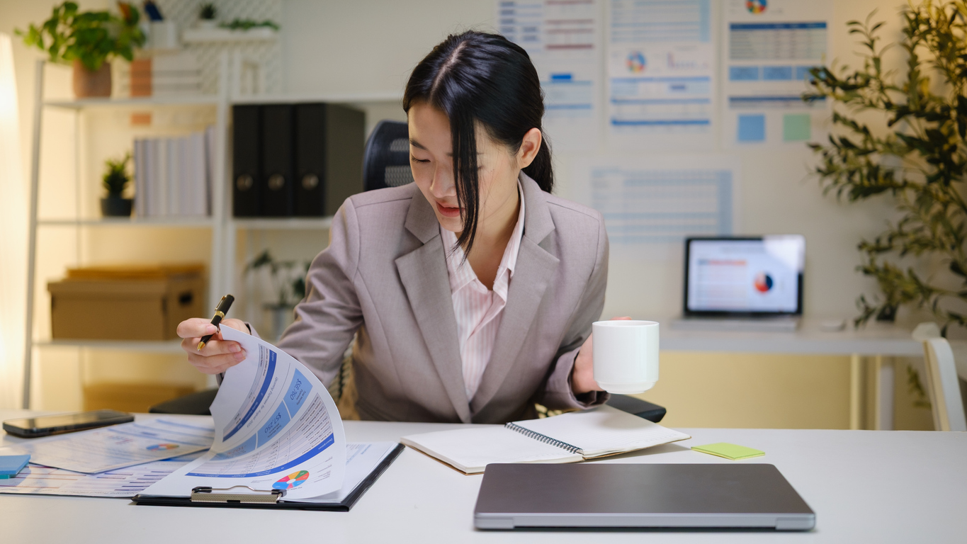 Businesswoman analyzing reports and taking notes during a productive work session in a bright workspace.