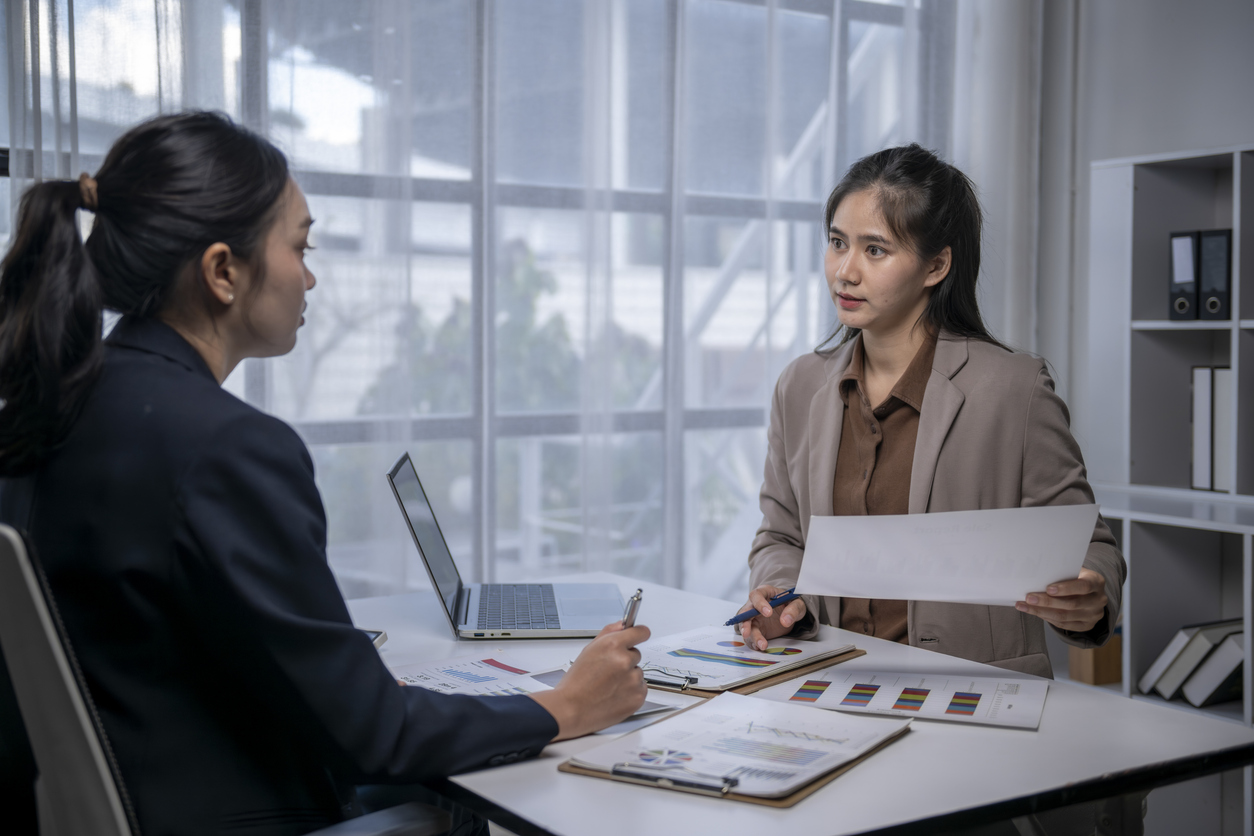 Two asian businesswomen discussing business strategy and financial charts in an office meeting
